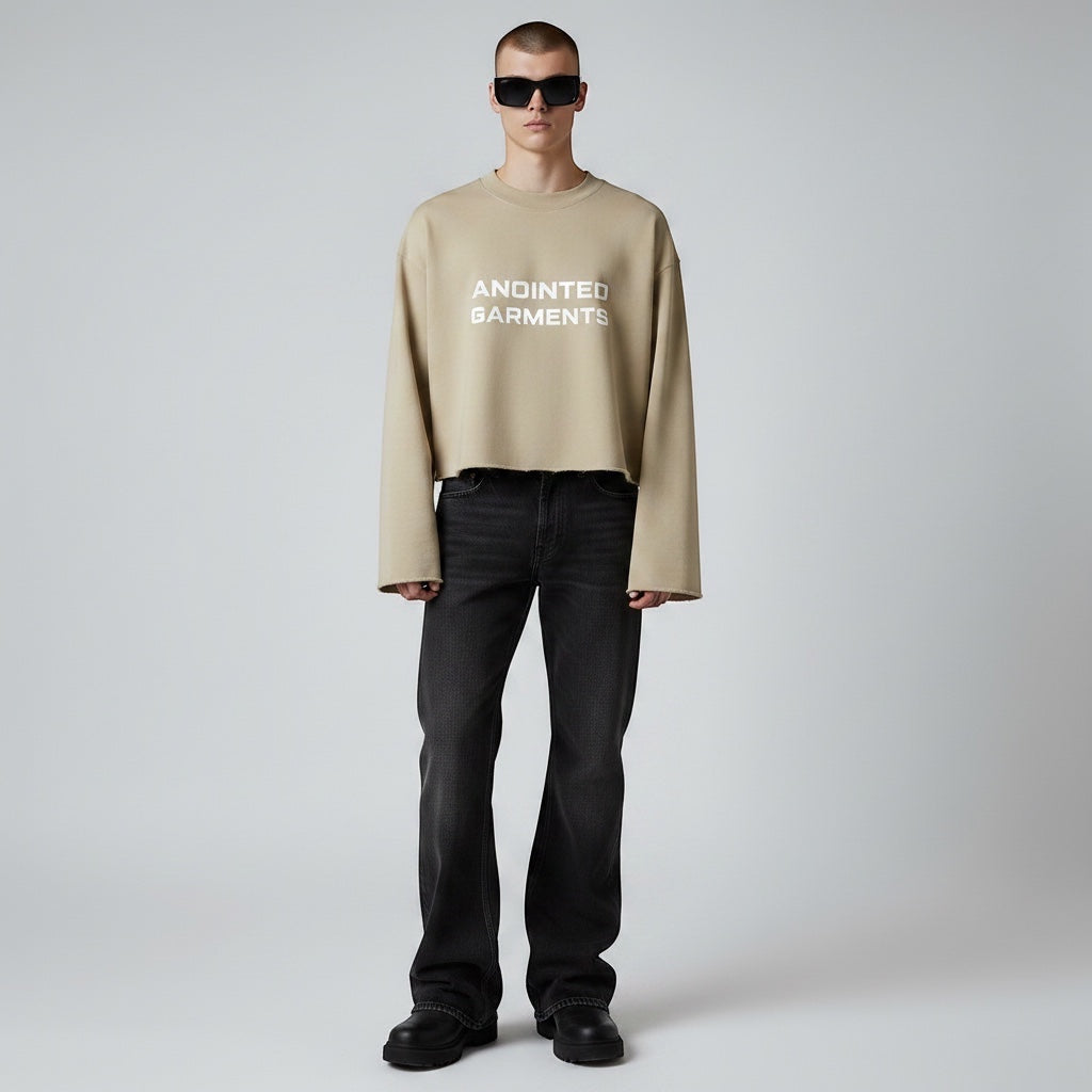 Model wearing Anointed Garments beige cropped crewneck sweatshirt with white chest branding and black jeans.