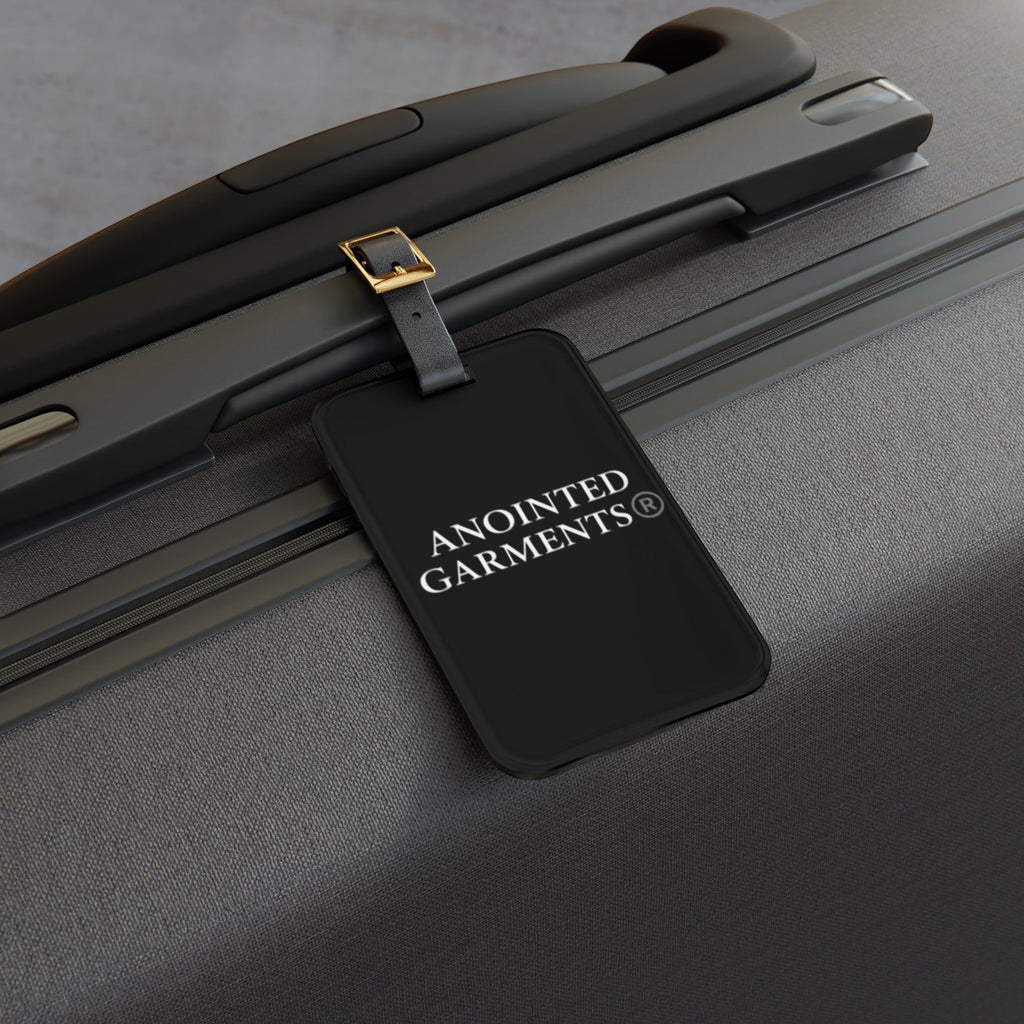 Anointed Garments black acrylic luggage tag with adjustable leather strap attached to a grey suitcase