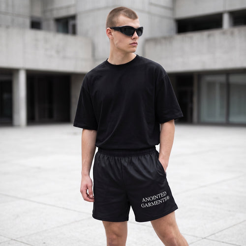 Anointed Garments unisex athletic shorts in black with white logo, worn by a man in a black t-shirt and sunglasses.