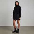 Model wearing Anointed Garments black denim mini skirt with gold-tone hardware, black turtleneck, and boots.