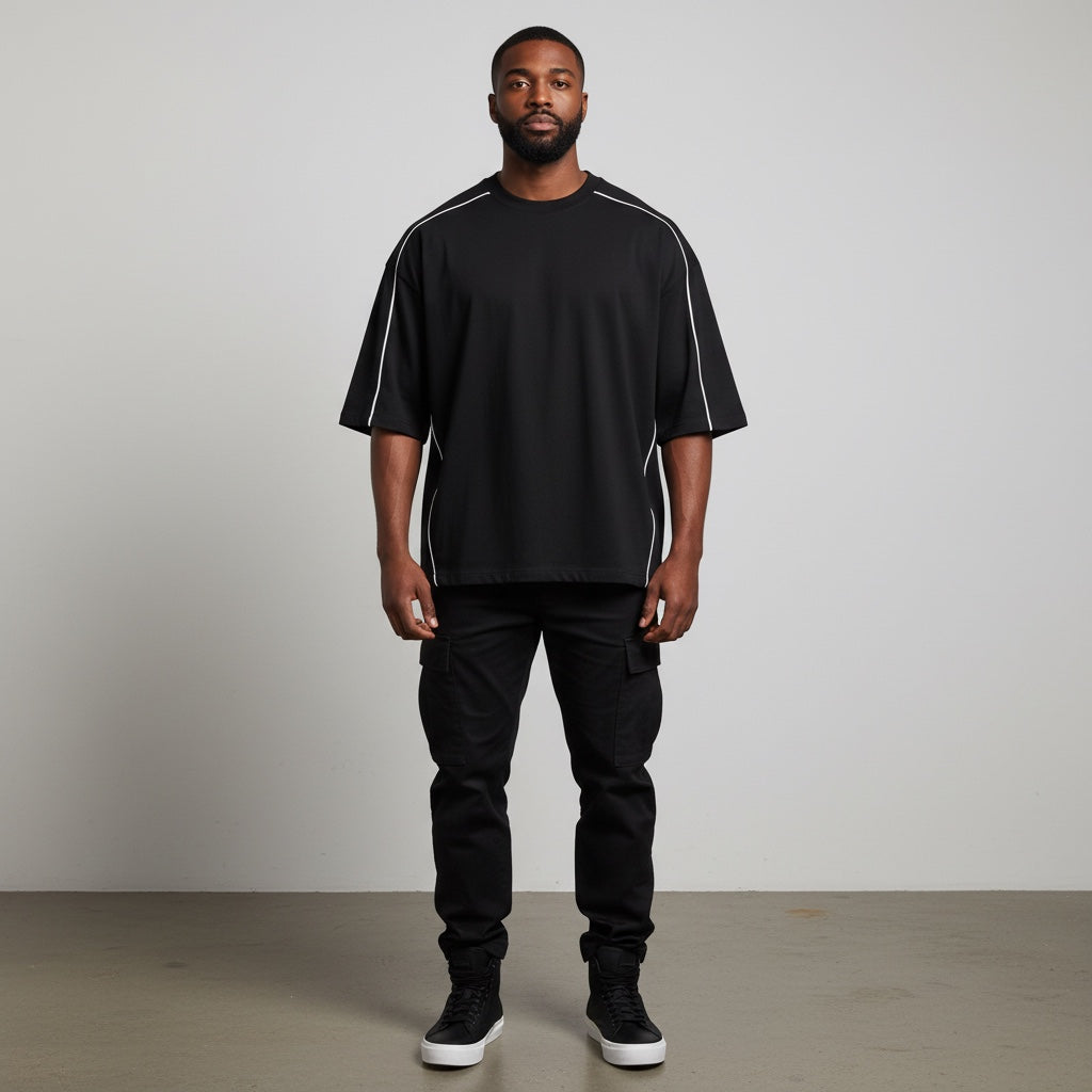 A man wearing an Anointed Garments black oversized cotton t-shirt with white piping detail on shoulders and sides.