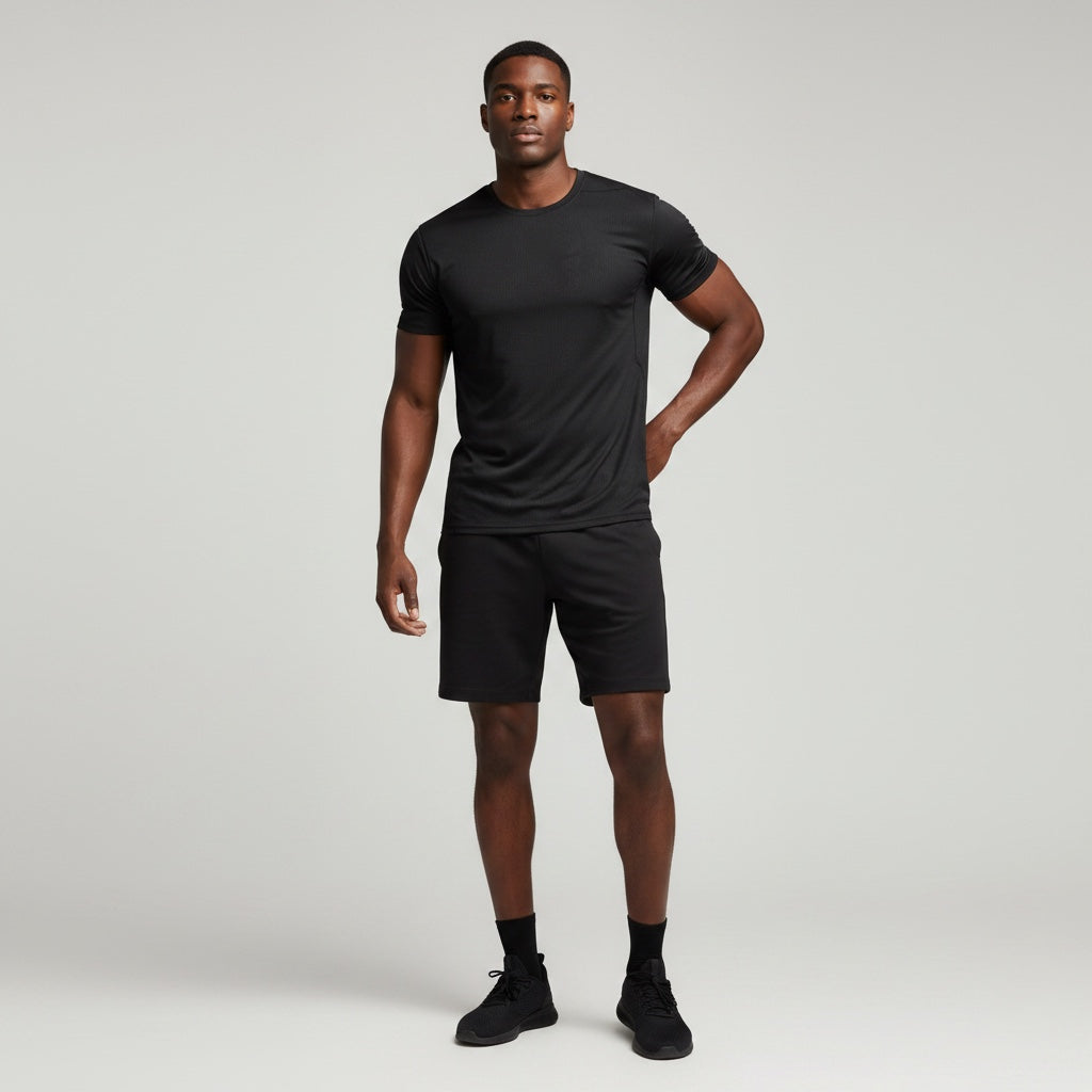 A man wearing an Anointed Garments black performance crew neck t-shirt and matching shorts in a studio setting.