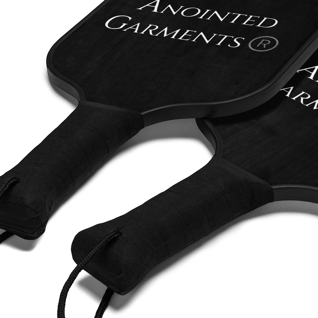 Anointed Garments pickleball paddle set featuring two black wooden paddles with comfortable poly-cotton handle grips.