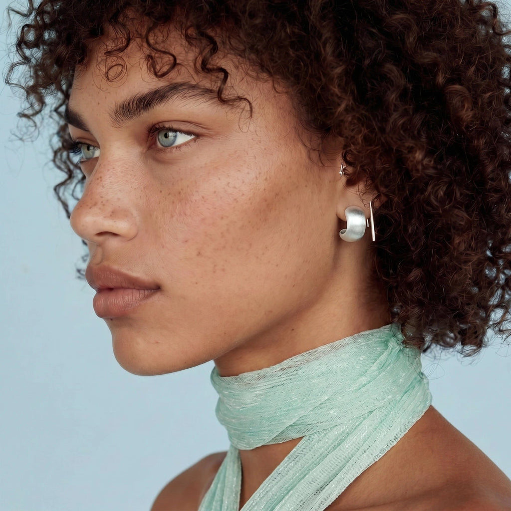 Anointed Garments brushed sterling silver geometric stud earrings worn by a model with curly hair and a mint scarf.