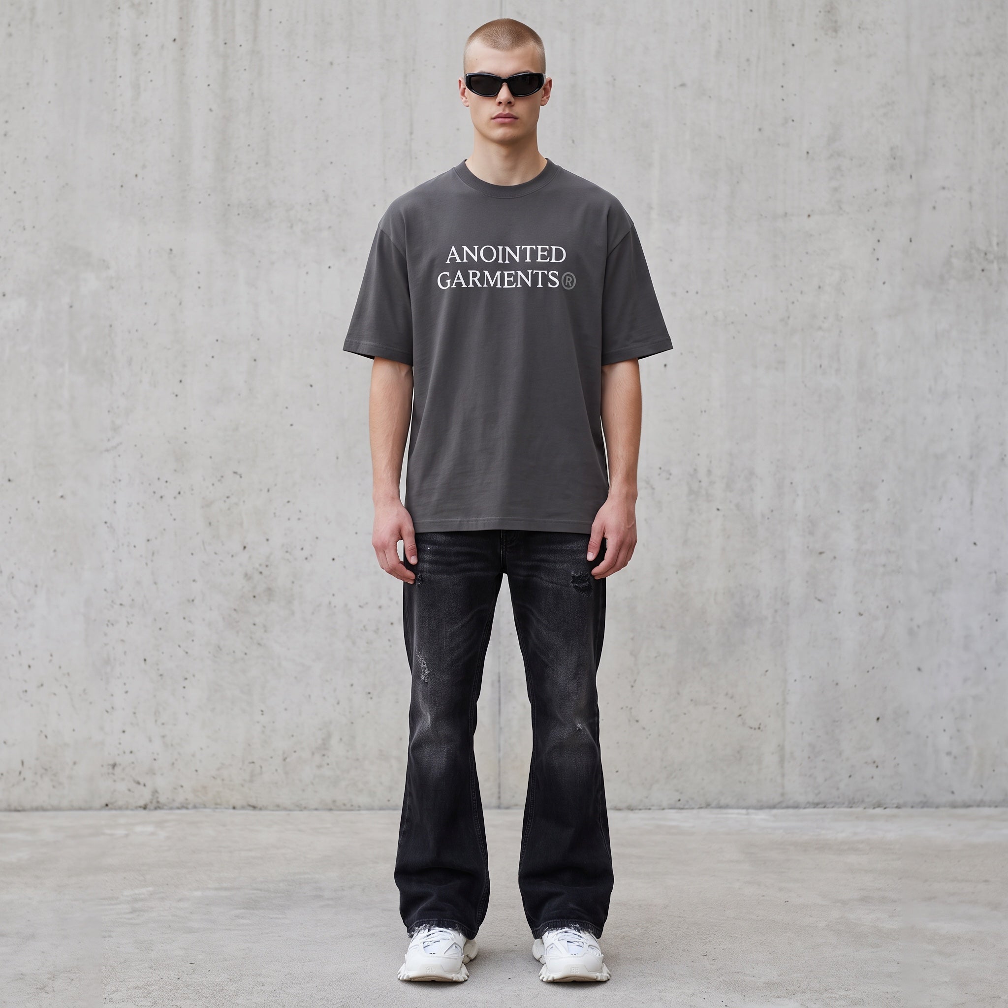 Model wearing an Anointed Garments charcoal grey boxy cotton t-shirt with white logo, black jeans, and sunglasses.
