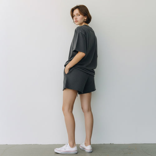 A woman wearing Anointed Garments charcoal grey cotton fleece lounge shorts with a raw-edge hem and side pockets.