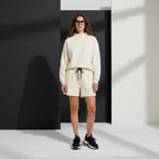 Woman wearing an Anointed Garments cream mock neck pullover sweatshirt and matching shorts against a geometric backdrop.