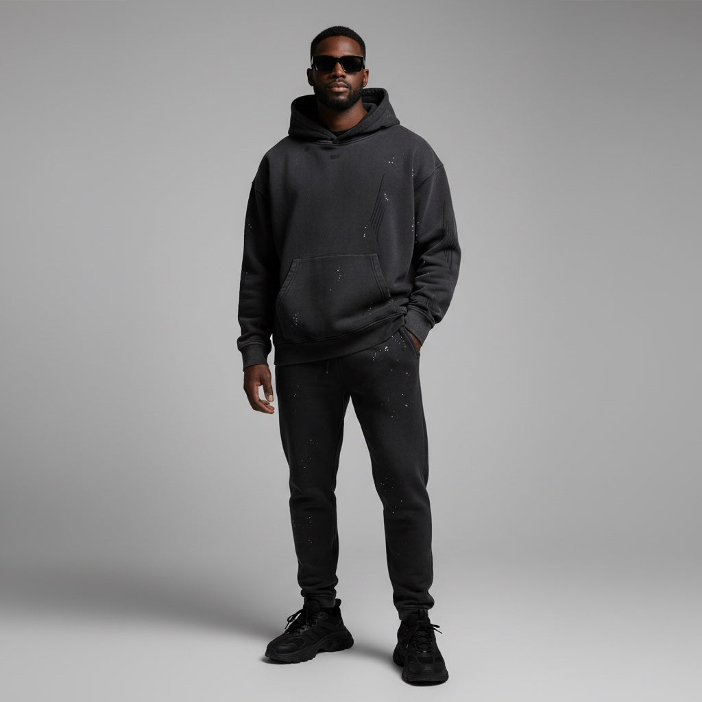 Man wearing Anointed Garments washed-black distressed pullover hoodie and matching sweatpants with paint splatter detail