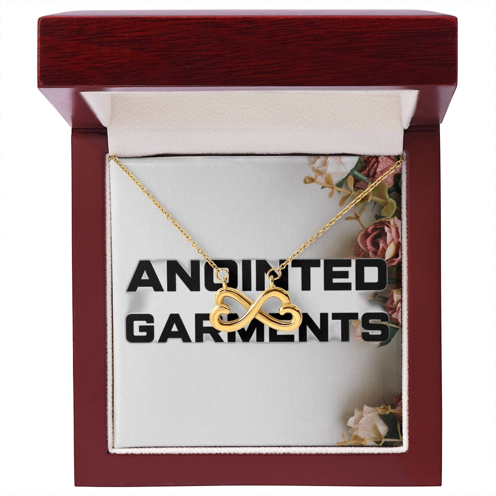 Anointed Garments gold heart infinity necklace in a polished wooden gift box with floral background.