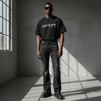 A model wearing an Anointed Garments black cotton t-shirt with white Hebrew script graphic, paired with dark jeans.