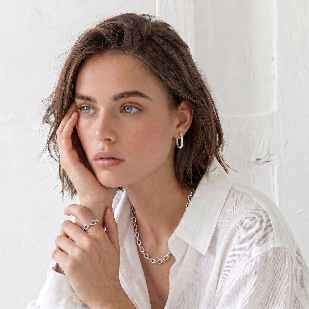 Anointed Garments platinum-plated sterling silver huggie hoops worn by a woman in a white shirt