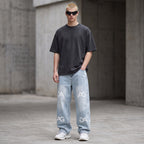 Model wearing Anointed Garments light-wash relaxed fit denim jeans with repeating AG logo print and grey t-shirt