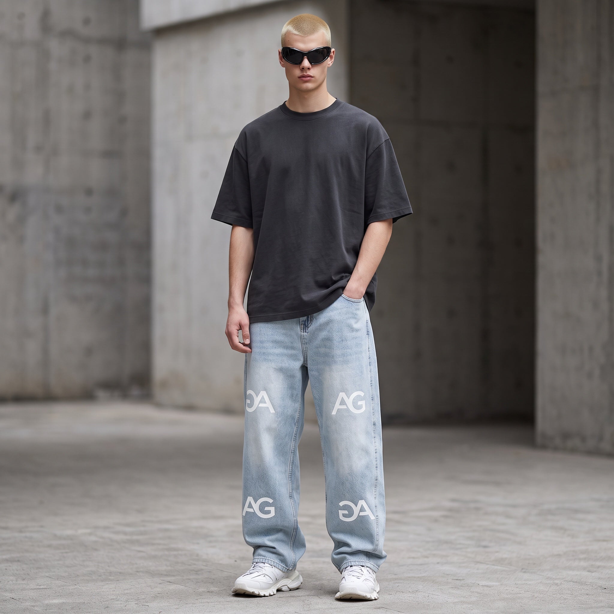 Model wearing Anointed Garments light-wash relaxed fit denim jeans with repeating AG logo print and grey t-shirt
