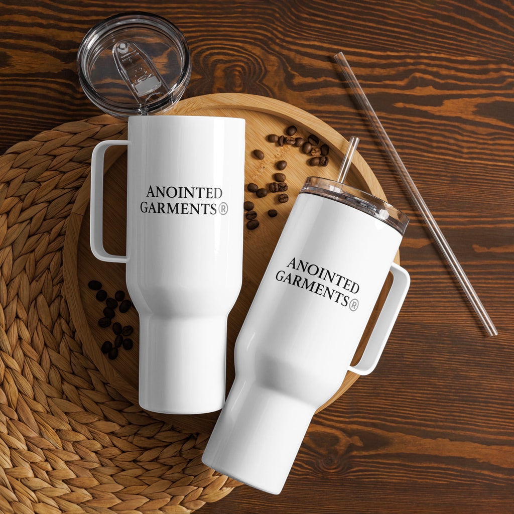 Two white Anointed Garments stainless steel travel mugs with handles, lids, and a straw on a wooden tray with coffee beans.